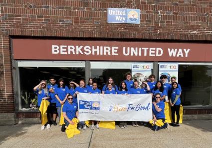 many students standing in front of office windows holding rakes and brooms